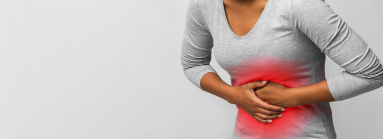 Mulher sentada com dor abdominal, segurando a barriga, ilustrando sintomas de Doença de Crohn tratados com Humira (adalimumabe), medicamento de alto custo que pode ser obtido pelo SUS ou plano de saúde.